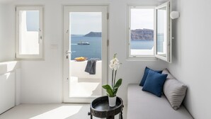 Una habitación con vistas al mar, una puerta que da al exterior, un sofá con almohadones y una planta en maceta.