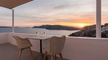 Un balcón con dos sillones de mimbre y una mesa, con vistas a una puesta de sol en la costa.