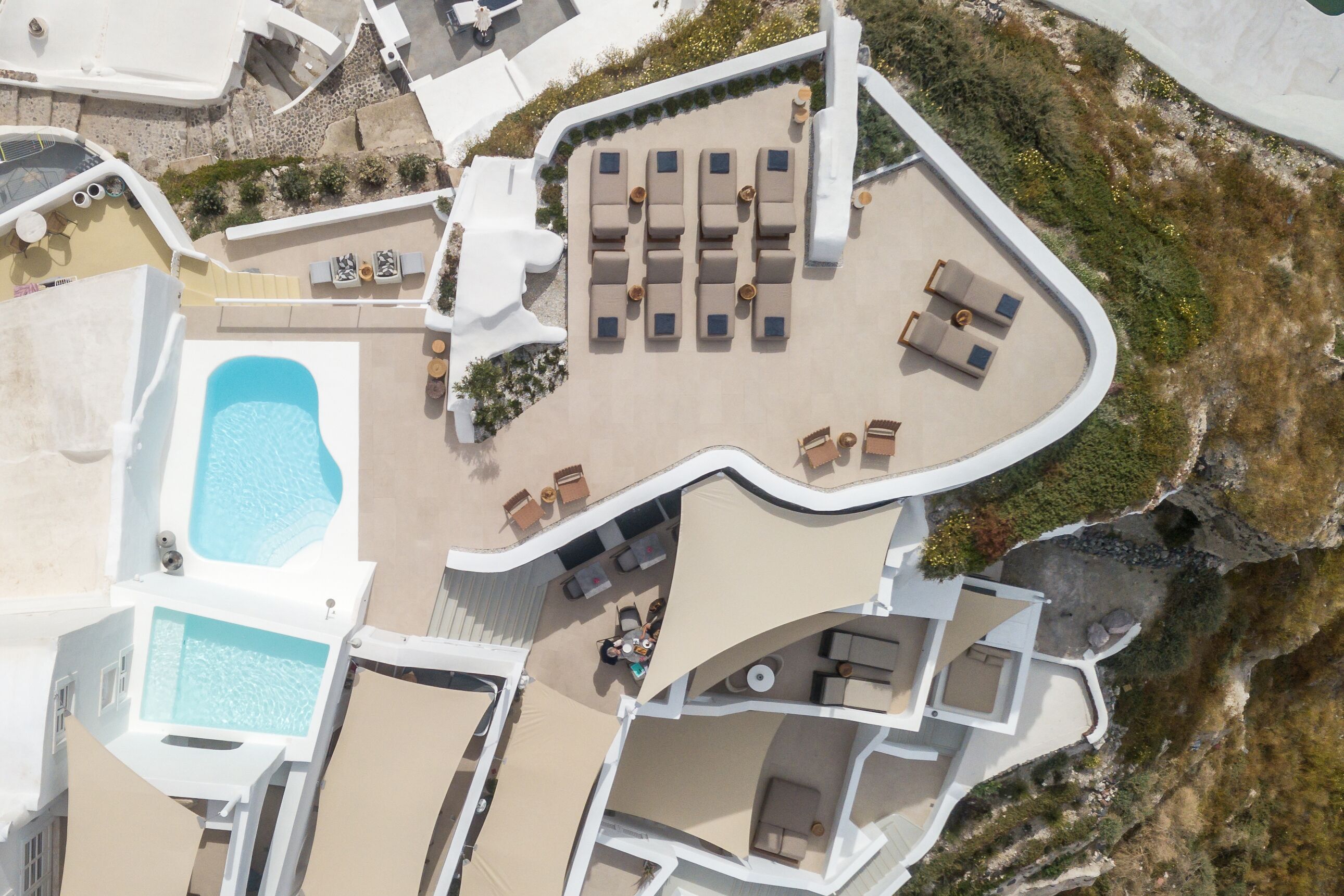 An aerial view of a resort with a swimming pool, sun loungers, and a lounge area.