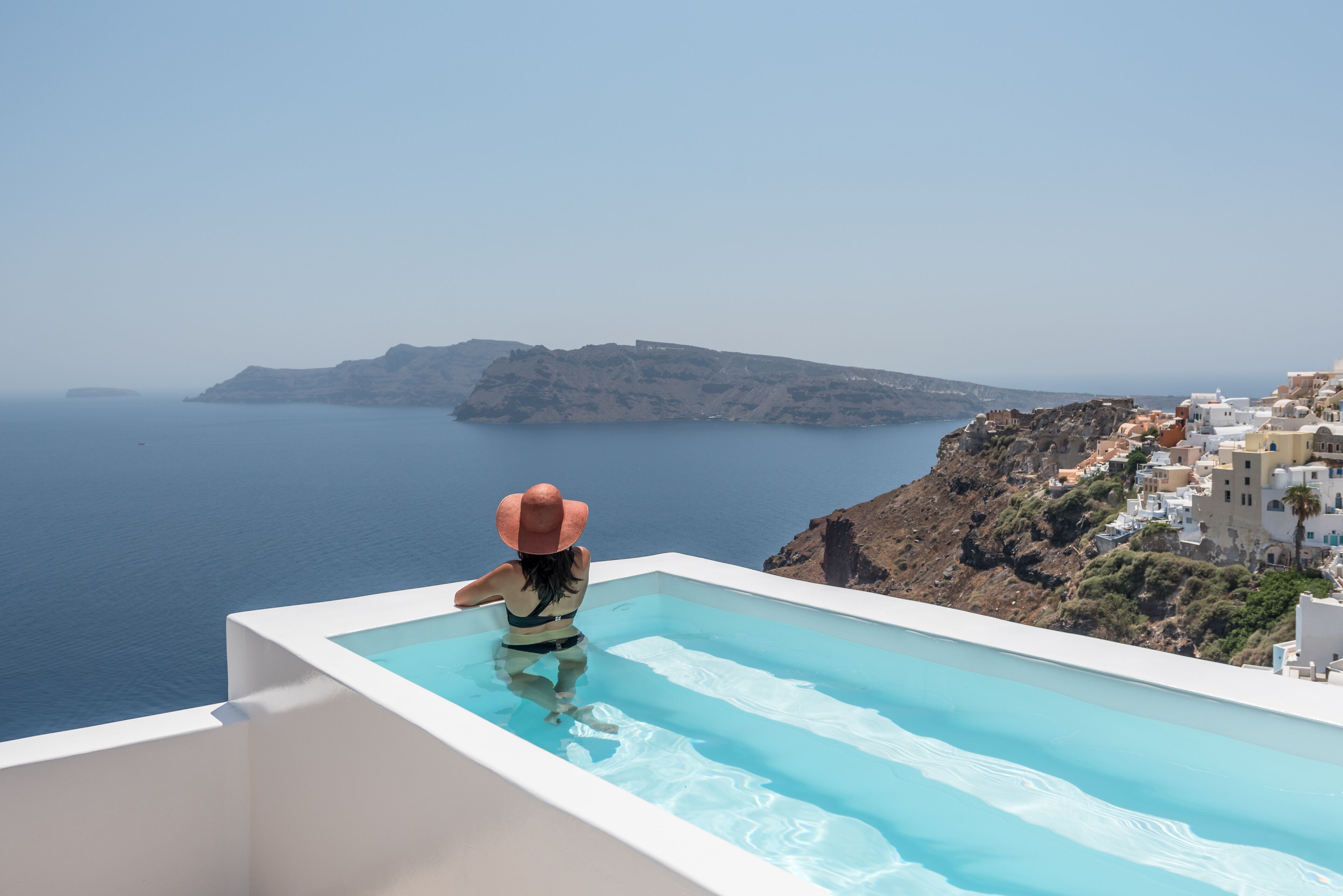 A person in a swimming pool with a view of the sea and a mountainous landscape.