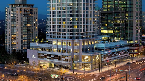 Un edificio de gran altura con varios balcones, fachada de vidrio moderna y un estacionamiento en la planta baja.