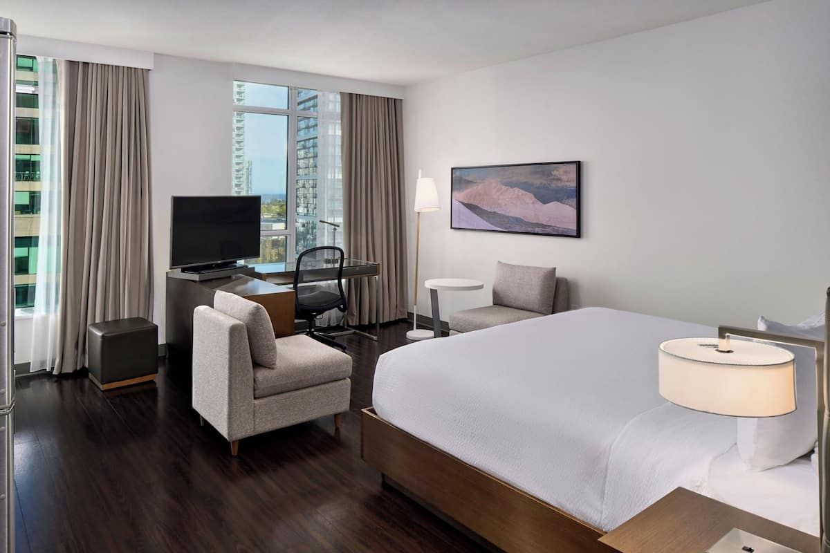 A hotel room with a large bed, a desk with a TV, a chair, a small table, and a painting on the wall.