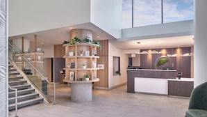 Un área de recepción moderna con una columna de madera central, un mostrador de recepción y una escalera.