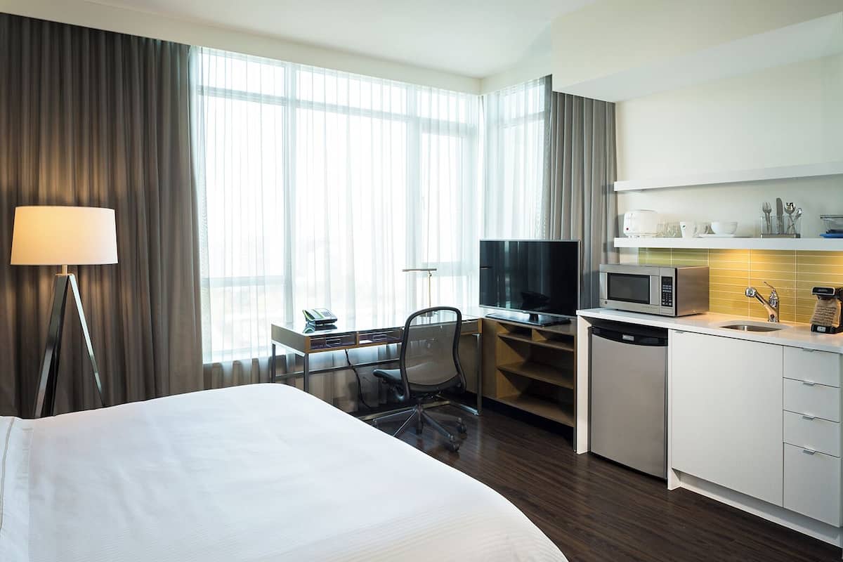 A hotel room with a bed, desk, TV, microwave, and kitchenette.