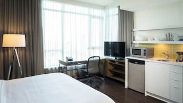 A hotel room with a bed, desk, TV, microwave, and kitchenette.