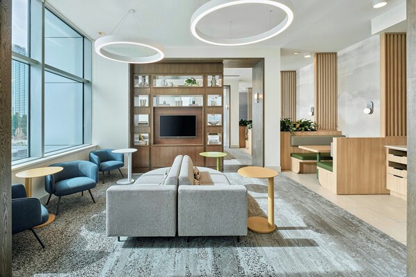 A modern office space with a grey sofa, blue chairs, a TV, and a wooden reception desk. - Element by Marriott Vancouver Metrotown (Burnaby)