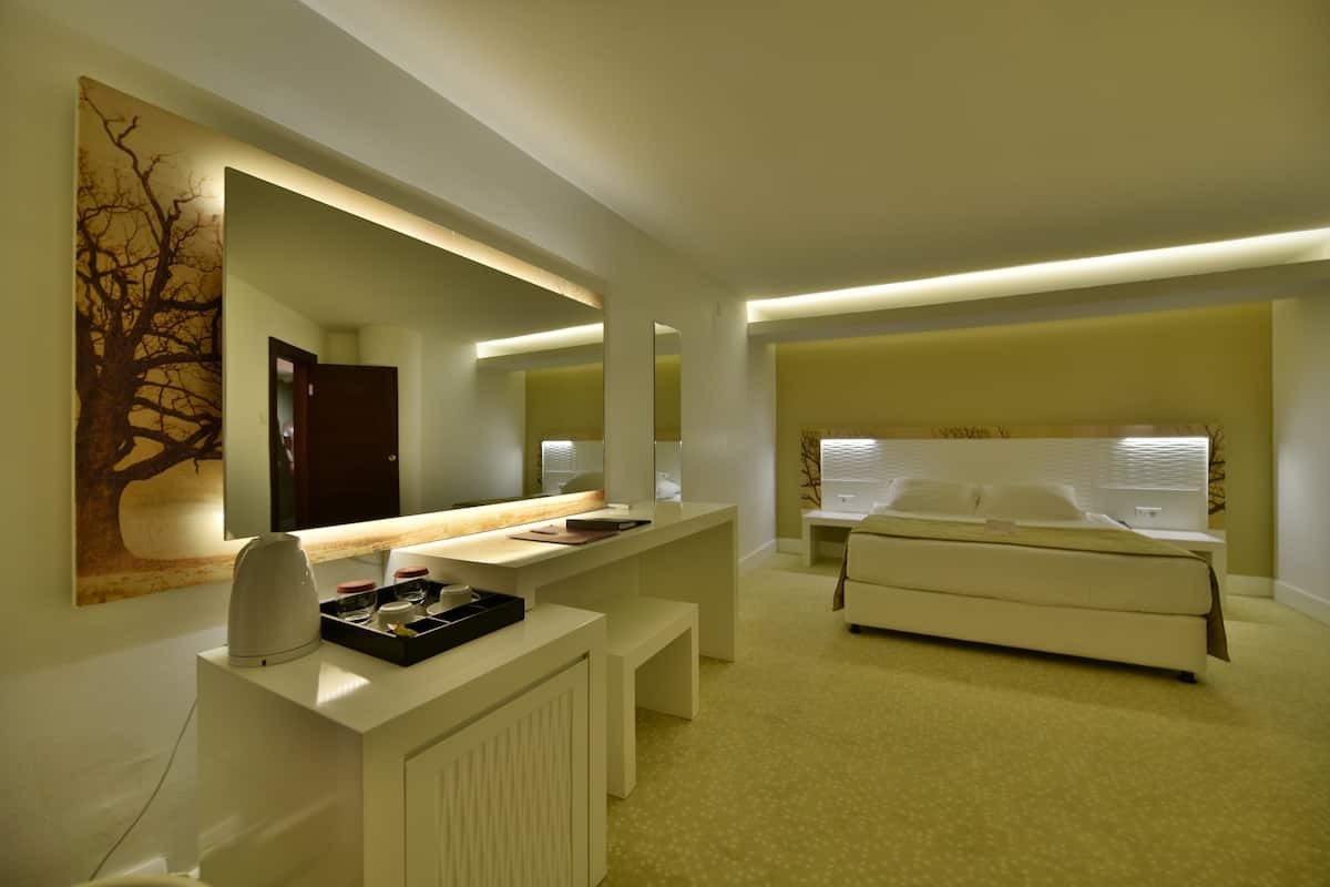 A modern bedroom with a large bed, a bedside table, a desk with a mirror, and a radiator.