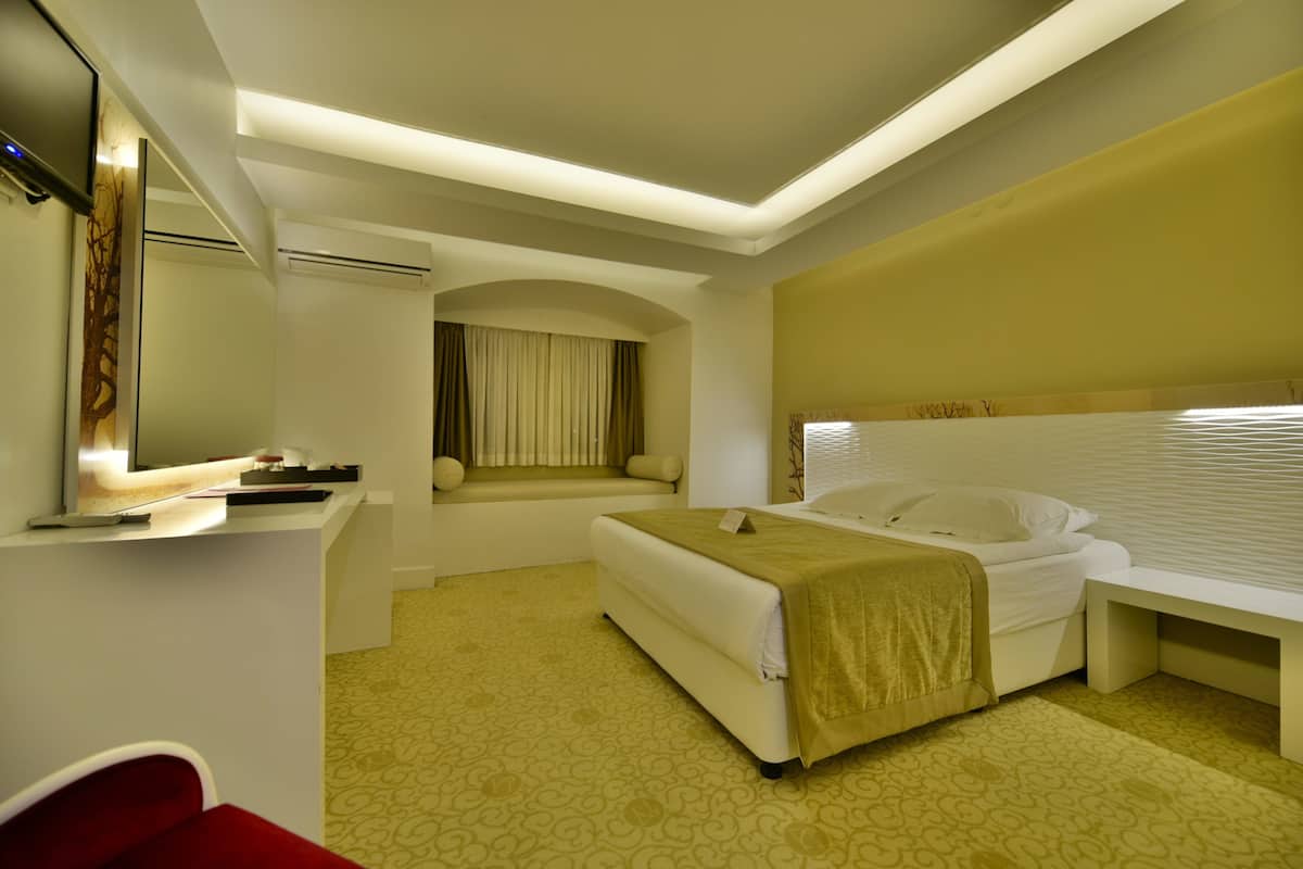 A hotel room with a bed, a bedside table, a mirror, and a window with curtains.