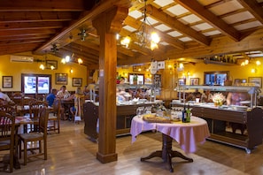 Restaurante com vigas de madeira, mesas, cadeiras e um espaço para buffet.