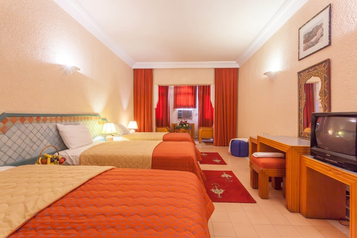 A hotel room with two beds, a desk with a television, and a small seating area.