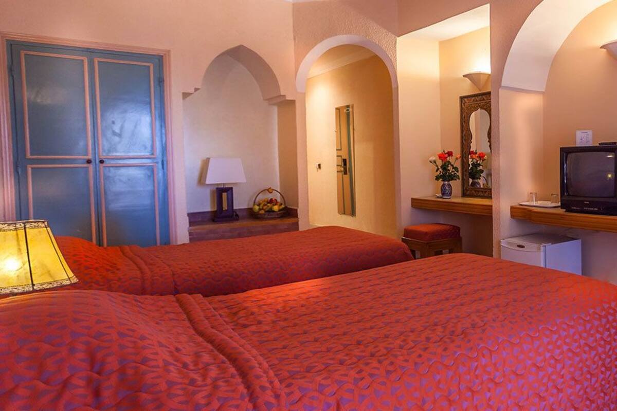 A hotel room with two beds, a television, a desk with a mirror, and a flower arrangement.