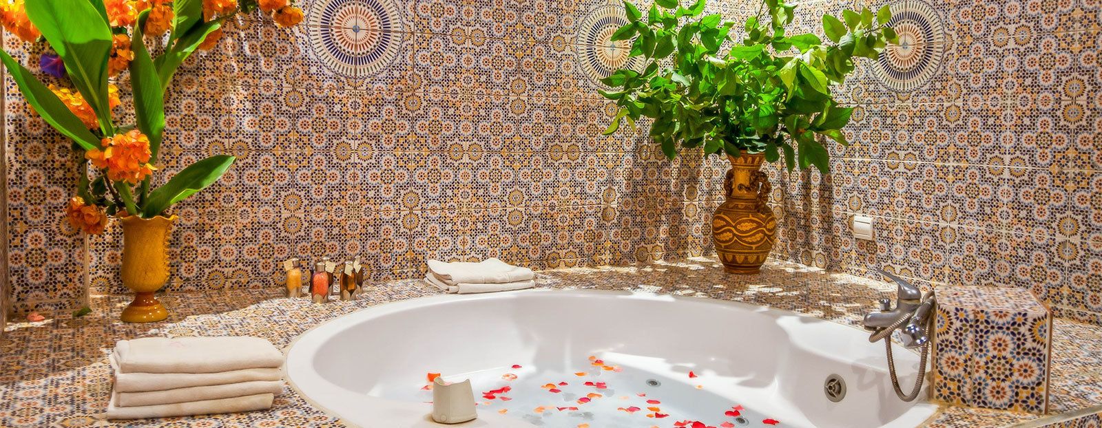 Une salle de bain avec une baignoire sur pieds, des carreaux décorés et deux vases ornés de fleurs.
