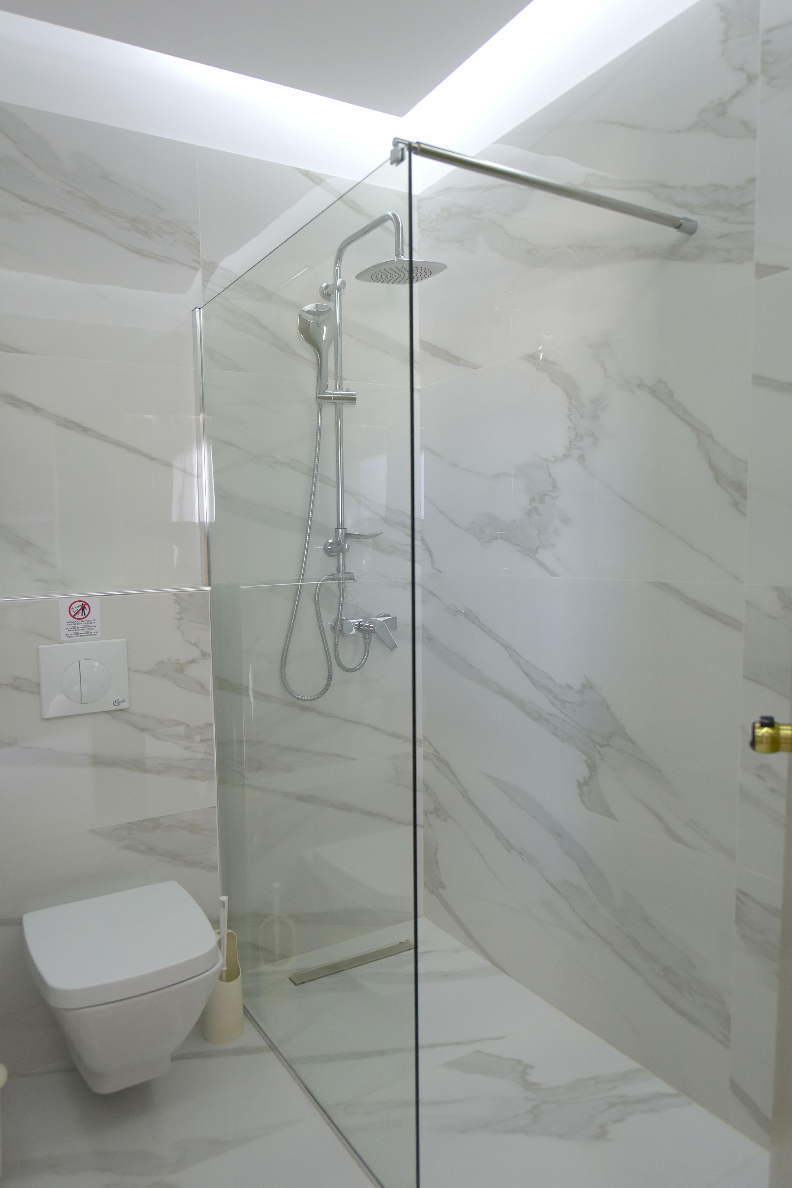 Ein modernes Badezimmer mit einer gläsernen Dusche, einer Toilette und Marmorwänden.