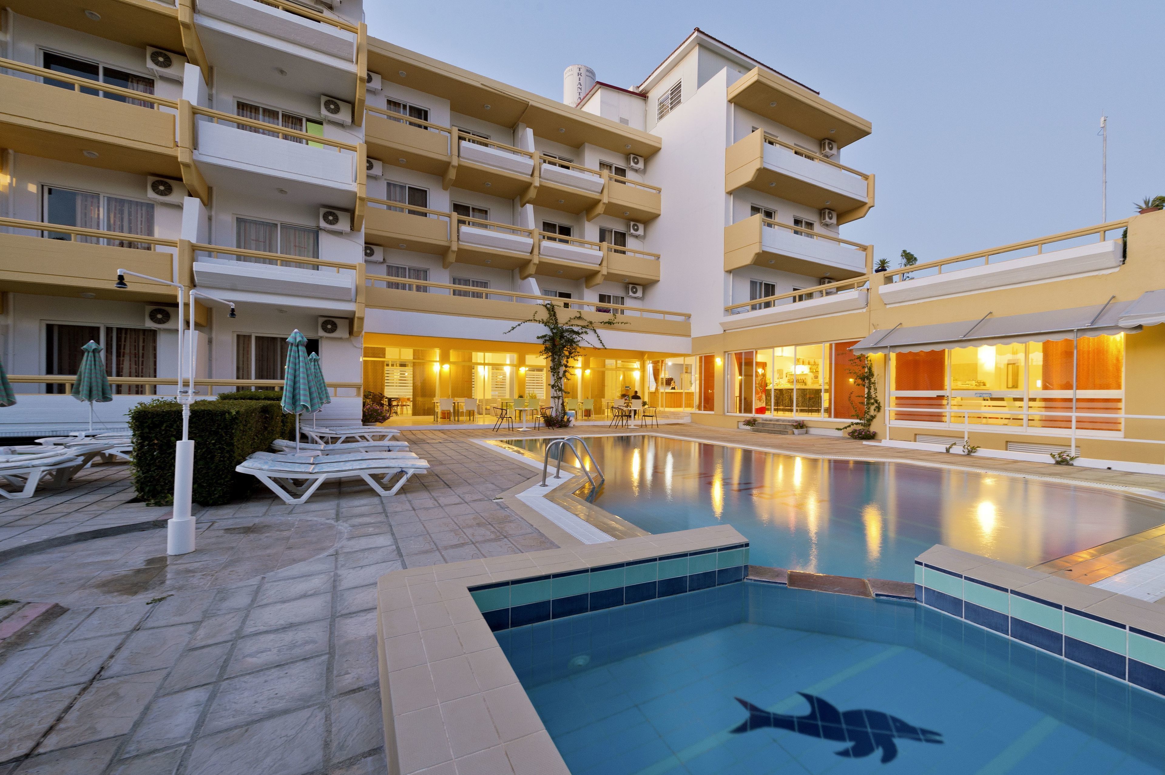 A hotel with a swimming pool, outdoor seating, and a well-lit building facade.