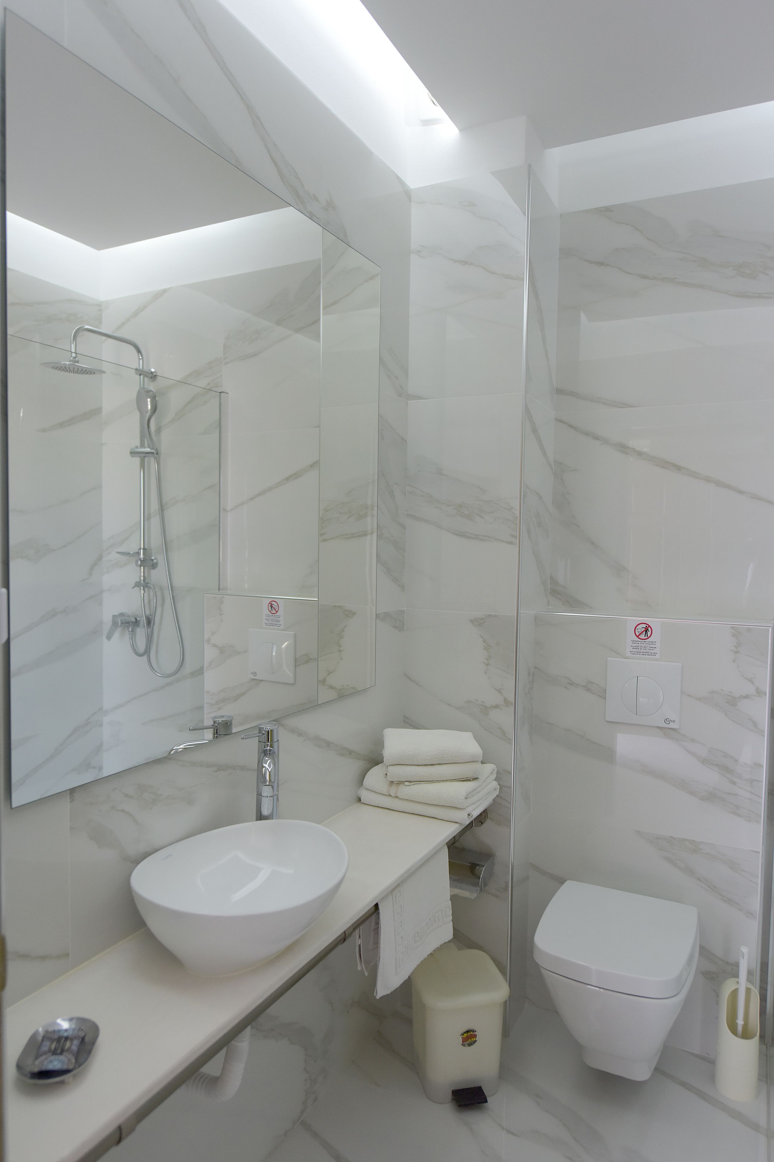 A modern bathroom with a white sink, a large mirror, a shower, and a toilet.