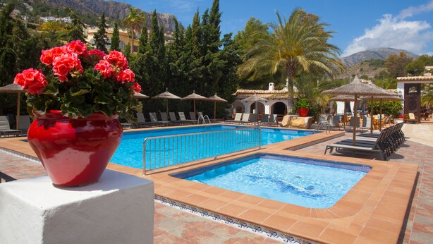 Un espace piscine agrémenté d’un pot de fleurs rouge, de chaises longues et offrant une vue sur les montagnes.