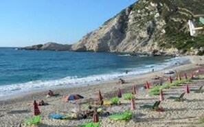 Une plage où des gens se prélassent au soleil et se baignent, une falaise rocheuse en arrière-plan, et des parasols alignés le long du rivage.
