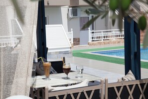 A poolside view with a table, drinks, and a glimpse of a pool and building. - Athinoula (Kos)