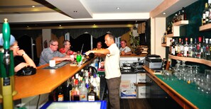 Eine Bar mit einem Barkeeper, der Getränke serviert, einer Theke mit verschiedenen Flaschen und einem Regal mit Spirituosen.