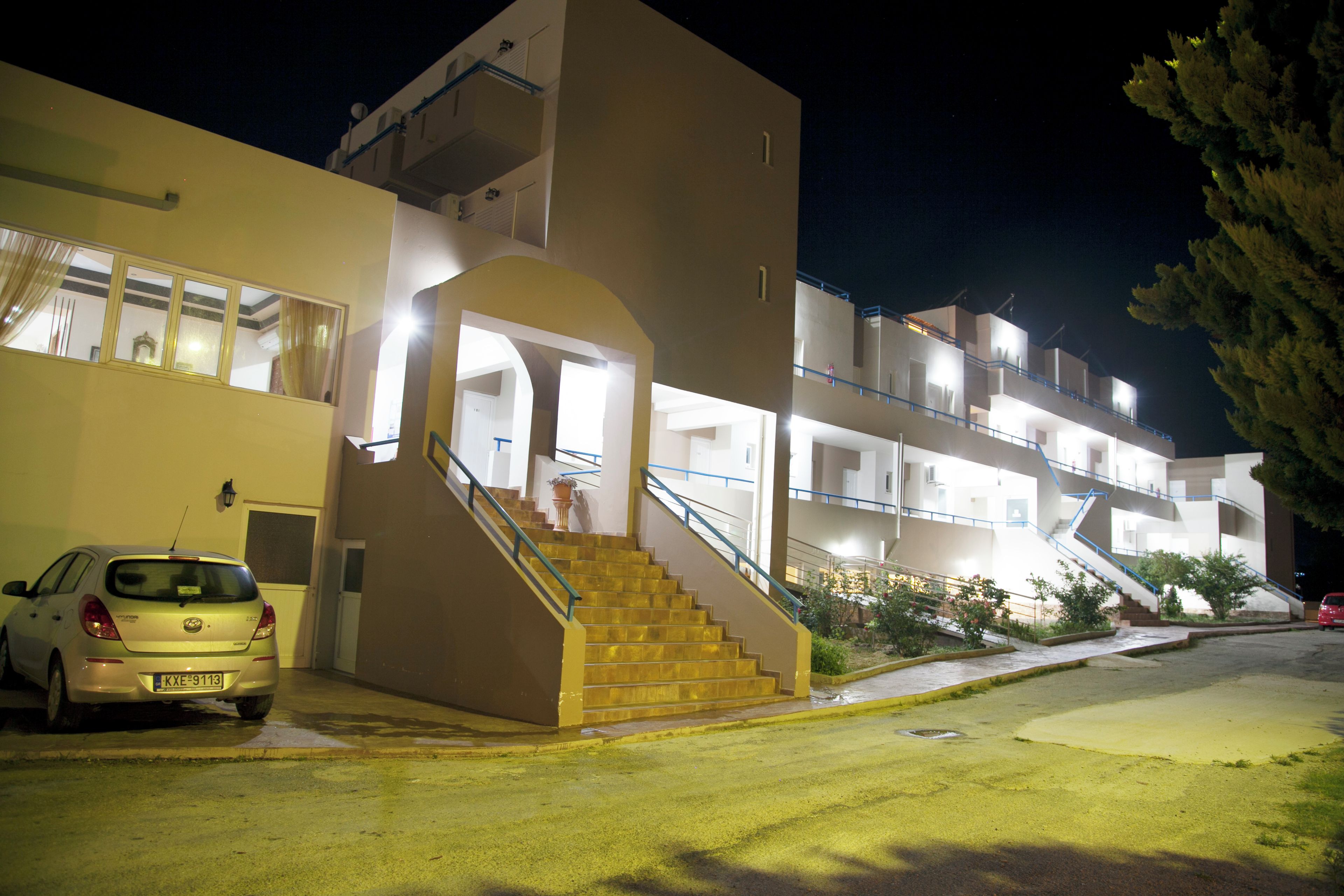 A multi-story building with a central staircase, a car parked in front, and a tree to the right.