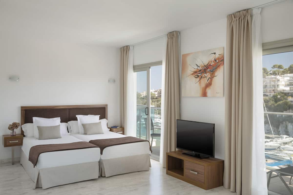 Quarto de hotel moderno com uma cama grande, televisão e varanda com vista para barcos.
