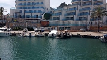 A marina with several boats docked, a modern building with multiple balconies, and a clear sky.