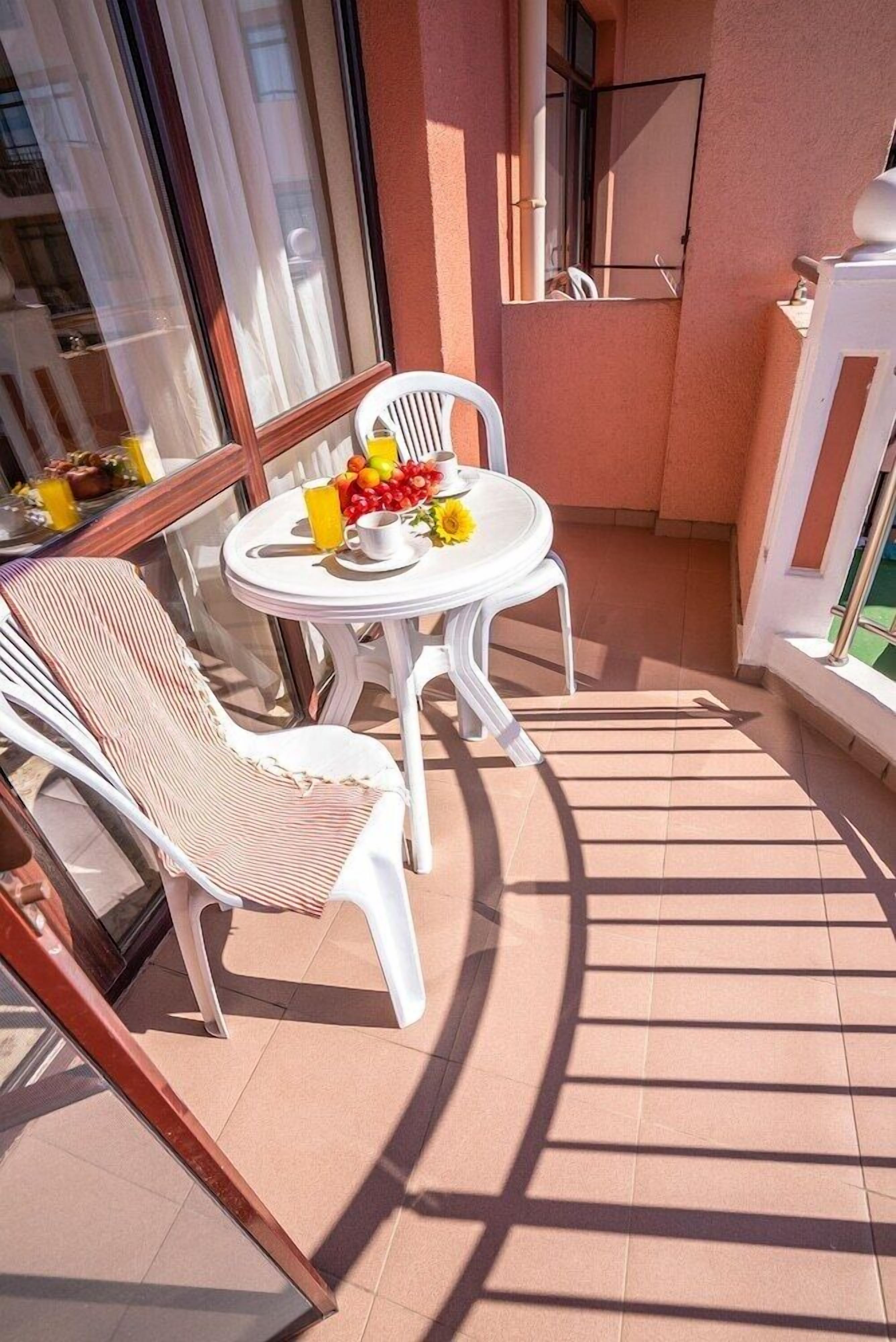 A small balcony with a round table and two chairs, a glass door, and a view of the building's interior.