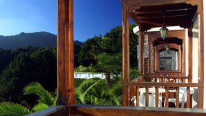 Ein hölzerner Pavillon mit einer Steinmauer und Blick auf üppiges Grün sowie Berge im Hintergrund.