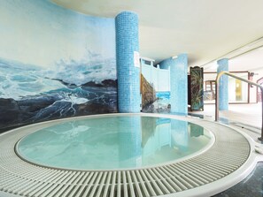 Kylpyläalue, jossa on seinämaalaus, joka esittää valtameren aaltoja, laatoitetut pylväät ja lasiseinillä varustettu poreallas.