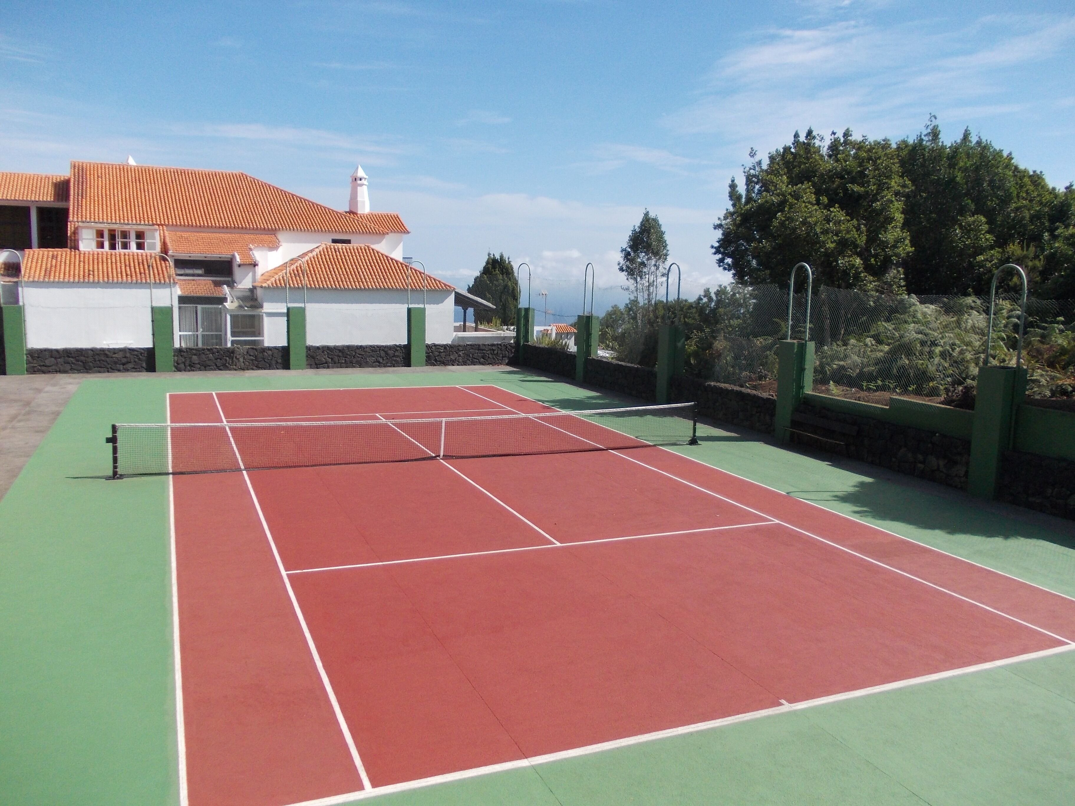 Ein Tennisplatz mit Netz, umgeben von einem grünen Zaun und einer Steinmauer.