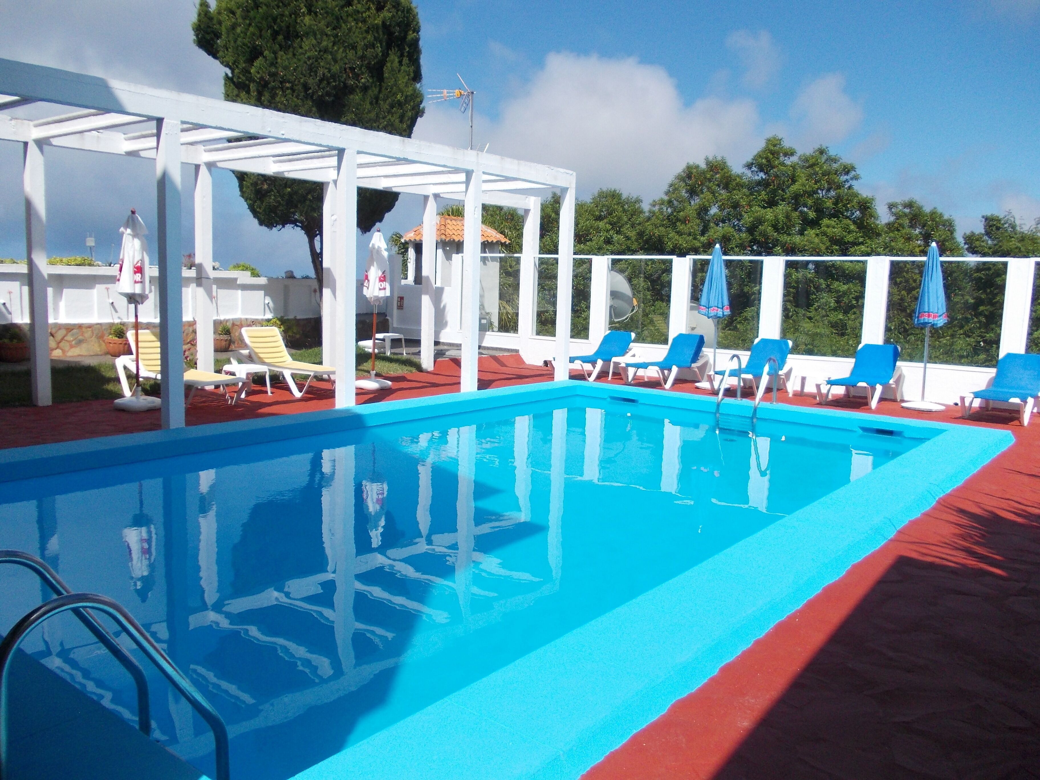 Ein Swimmingpool mit blauem Wasser, umgeben von weißen Liegestühlen und Sonnenschirmen.