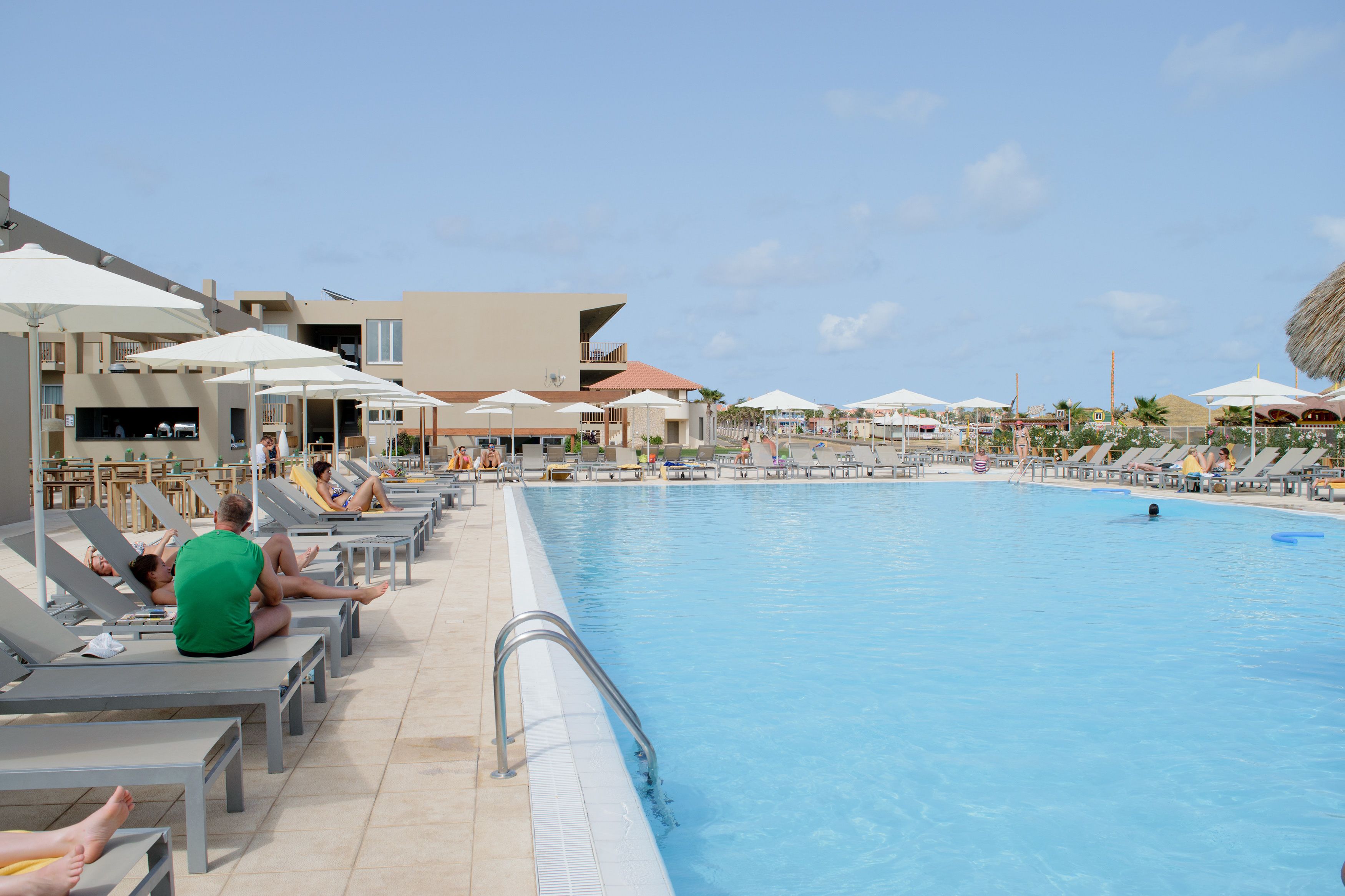 Un espace piscine aménagé avec des chaises longues et des parasols, entouré d’immeubles dotés de balcons.