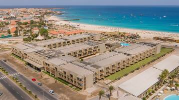 A hotel with multiple floors, a swimming pool, and a beach view.