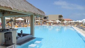 Zwembad met ligbedden en parasols, een bar en een gebouw met balkons op de achtergrond.