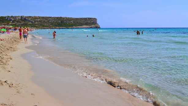 A beach with clear water, a sandy shore, and a rocky cliff in the background. - Villas Finesse (Alayor)