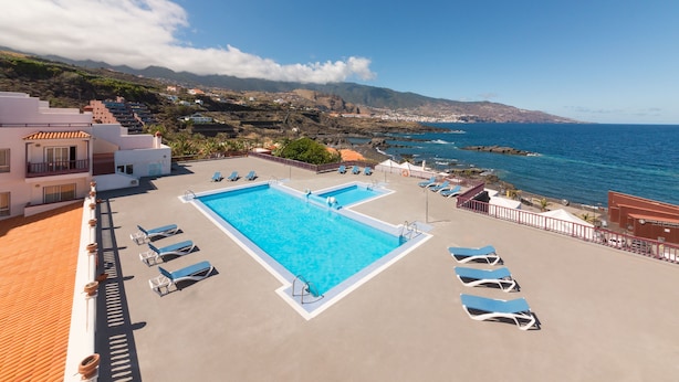 Una piscina en la azotea con varios sillones de sol y una vista despejada del océano y las colinas.