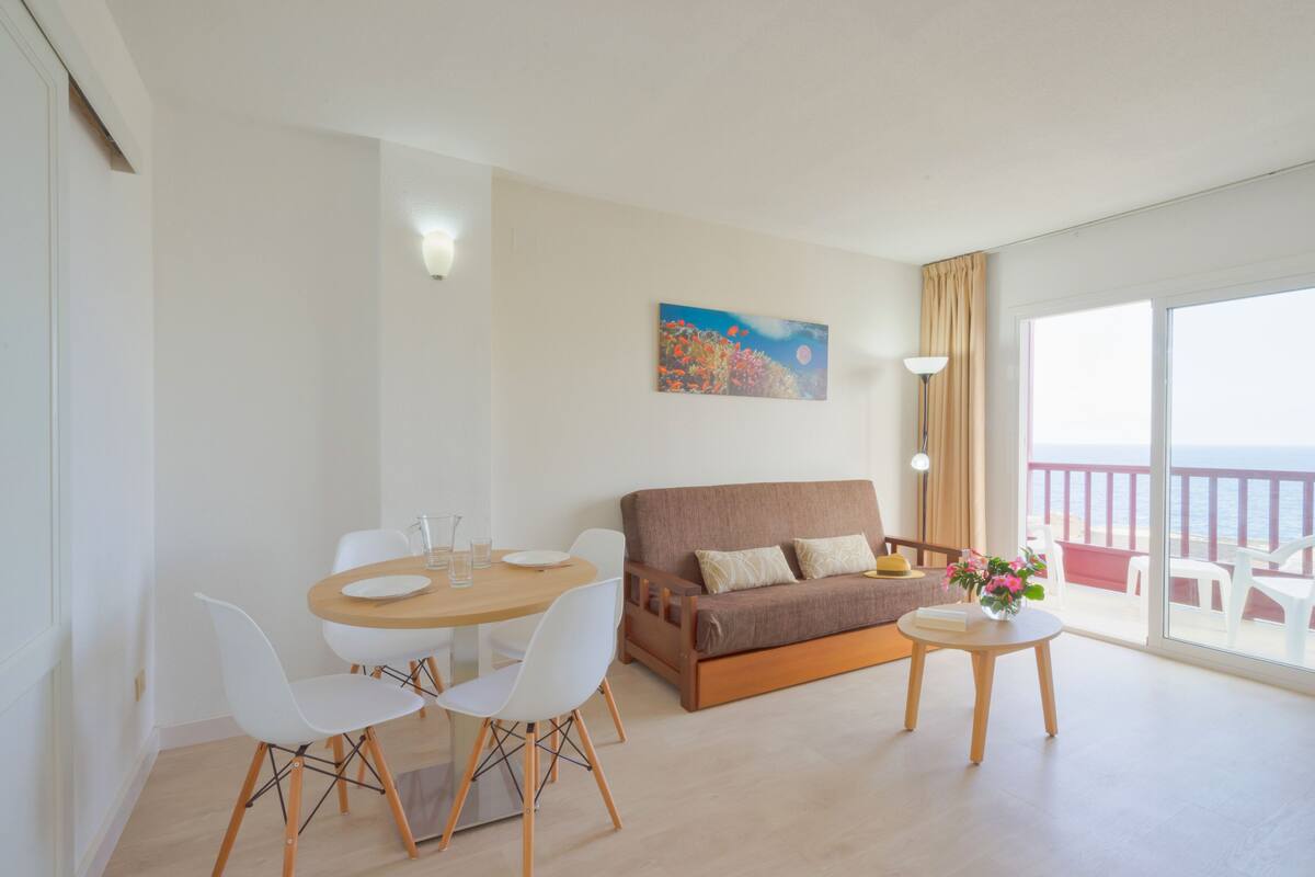 A modern living room with a sofa, dining table, chairs, and a balcony with a view.