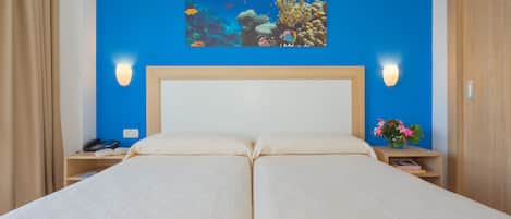 A double bed with a blue wall and two bedside tables, one with a phone and the other with a vase of flowers.