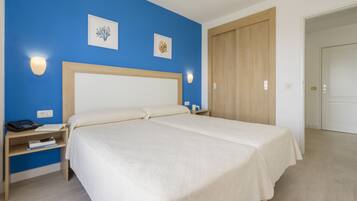 Una habitación de hotel con una cama grande, una mesita de noche con un teléfono y libros, y un armario de madera.