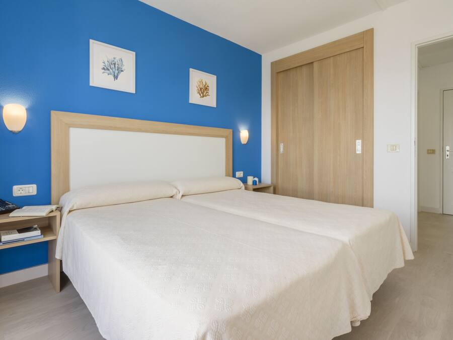 Una habitación de hotel con una cama grande, una mesita de noche con un teléfono y libros, y un armario de madera.