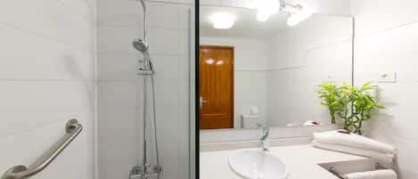 A bathroom with a shower, sink, mirror, and a potted plant.