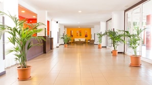 Un vestíbulo de hotel con suelo de baldosas, plantas en macetas, un mostrador de recepción y un sofá.
