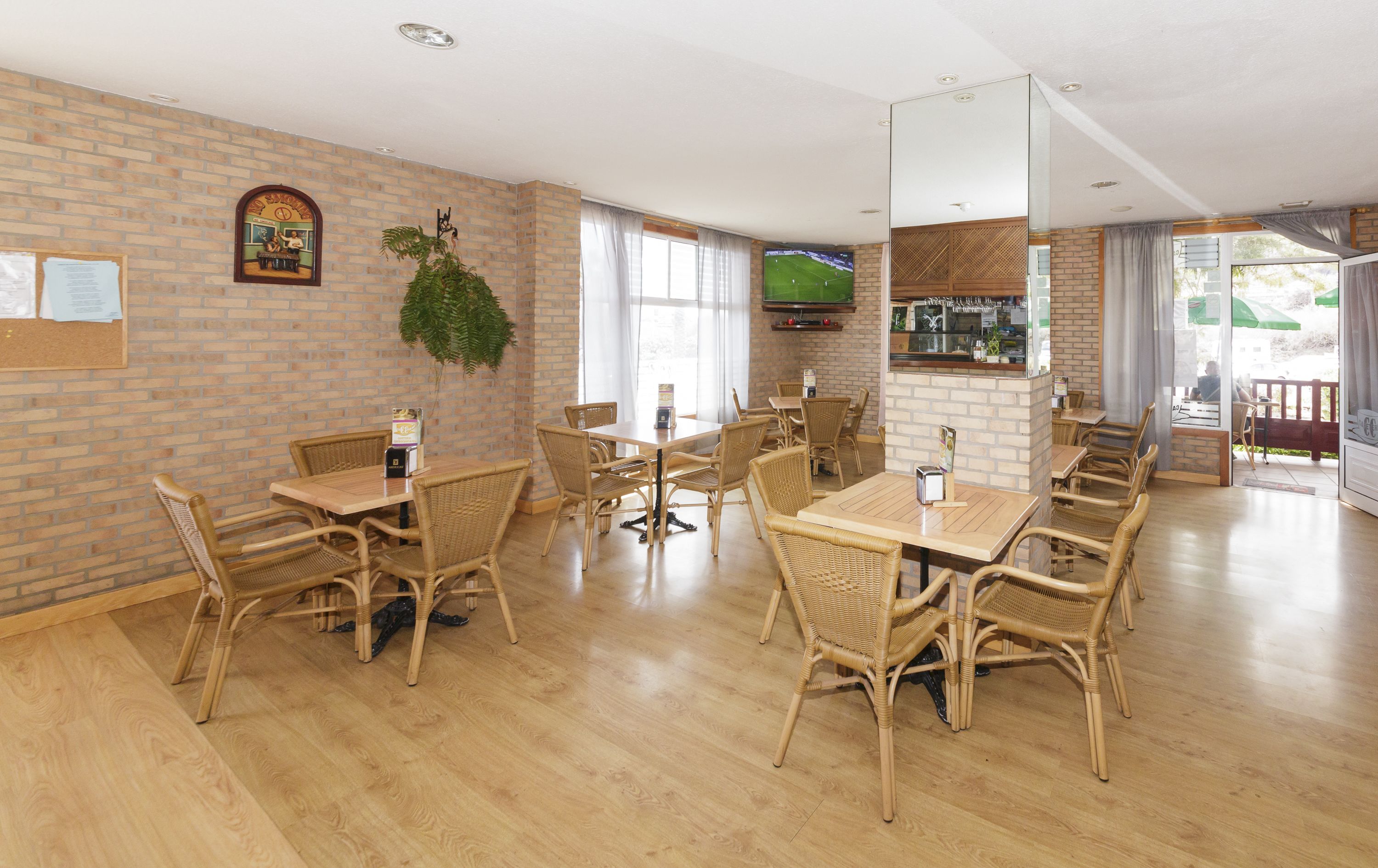 A spacious room with brick walls, wooden flooring, and wicker furniture. There is a television mounted on the wall and a plant hanging from the ceiling.