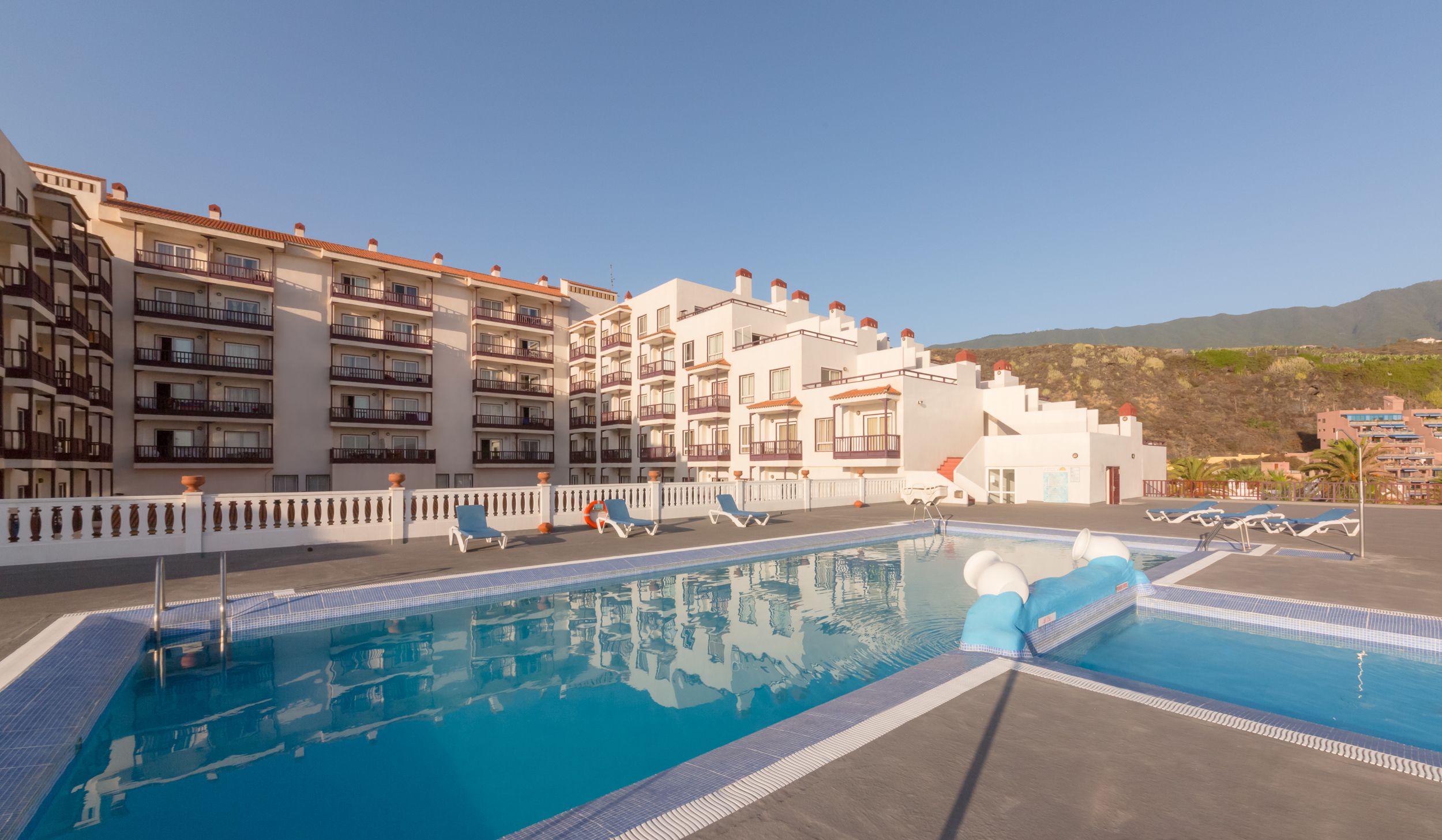A hotel with a swimming pool, multiple balconies, and a view of the surrounding landscape.