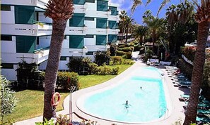 A swimming pool with a person in the water, surrounded by palm trees and a building with balconies. - Apartamentos Maba Playa (San Bartolomé de Tirajana)