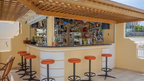 A bar area with a counter, stools, and a variety of items on shelves. - Cosmi Apartments by Estia (Hersonissos)