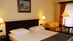 Habitación de hotel con cama doble, dos lámparas de noche, un sofá, una mesita y un cuadro en la pared.