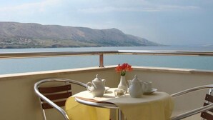 Una mesa con juego de té y un florero, en un balcón con vistas al agua y a las montañas.