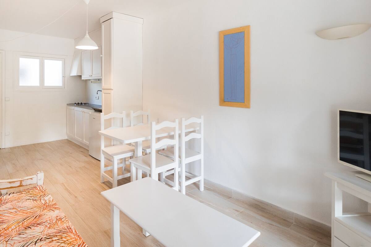 A modern kitchen with white cabinets, a dining area with white chairs and a table, and a television on a stand.