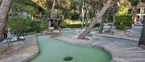 A miniature golf course with a green putting green, a hole, and surrounding stone walls.